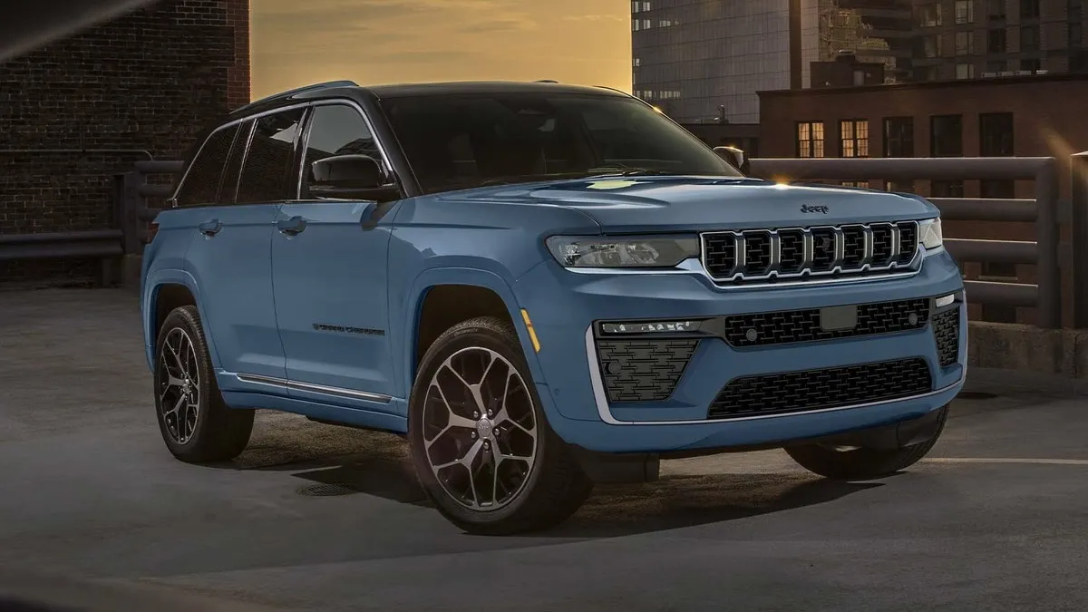 Front three-quarter view of a blue 2026 Jeep Grand Cherokee parked in the city in front of a modern building.
