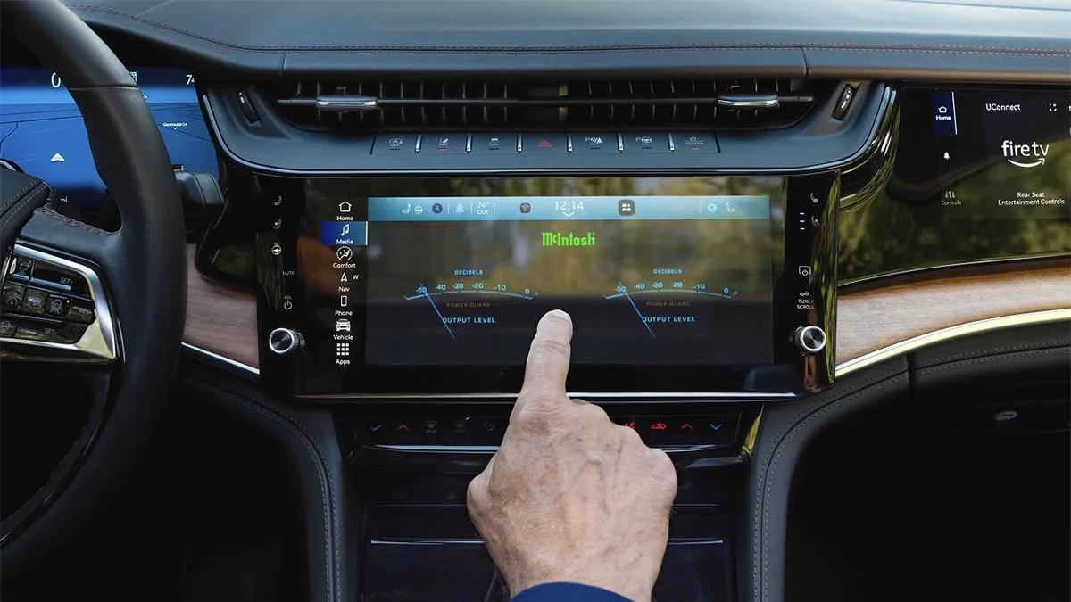 Close-up of the 2026 Jeep Grand Cherokee infotainment screen with a hand touching the touchscreen interface.
