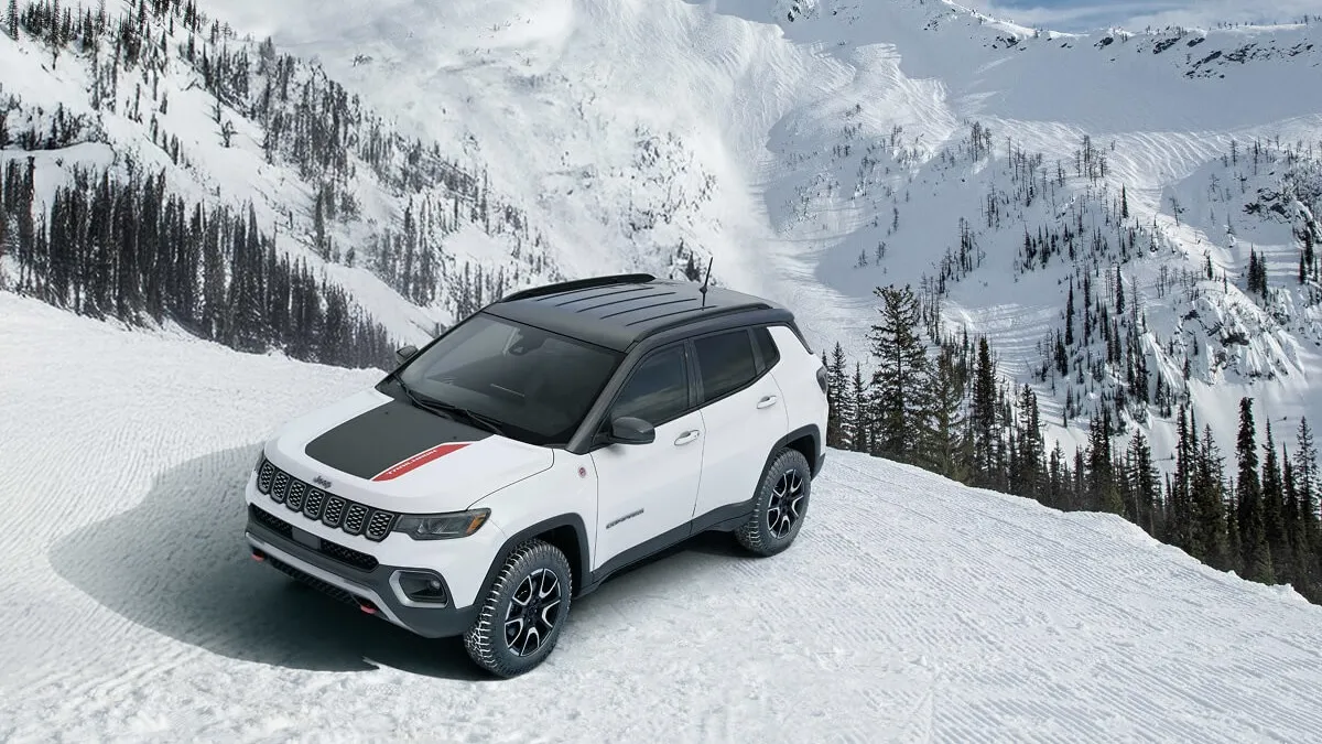Front three-quarter view of a white 2026 Jeep Compass parked on a snowy mountain with an alpine panorama.