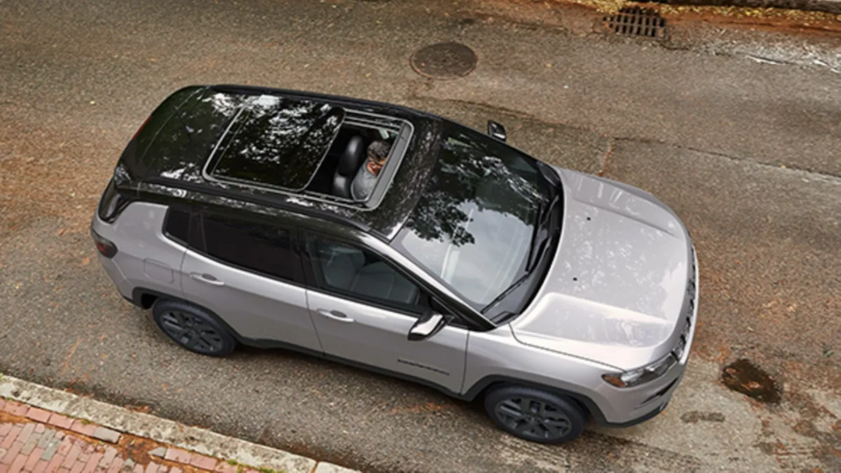 Aerial view of a gray 2026 Jeep Compass parked on a road with a natural landscape in the background.

